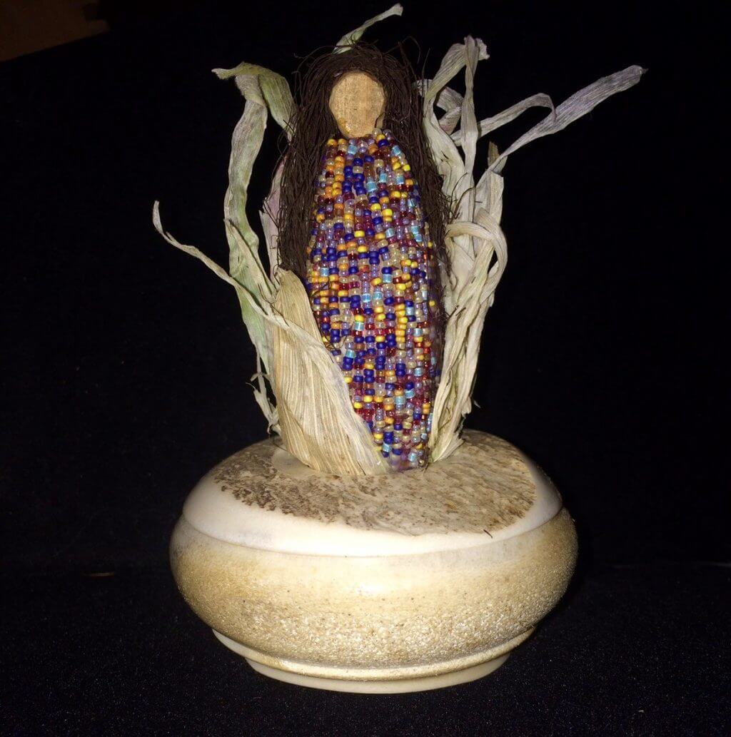Colorful beaded corn doll with corn husk dress on ceramic base