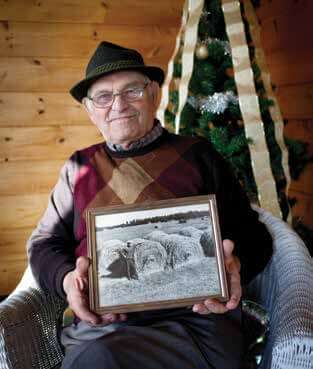 Elderly man in hat holding black and white photo near Christmas tree