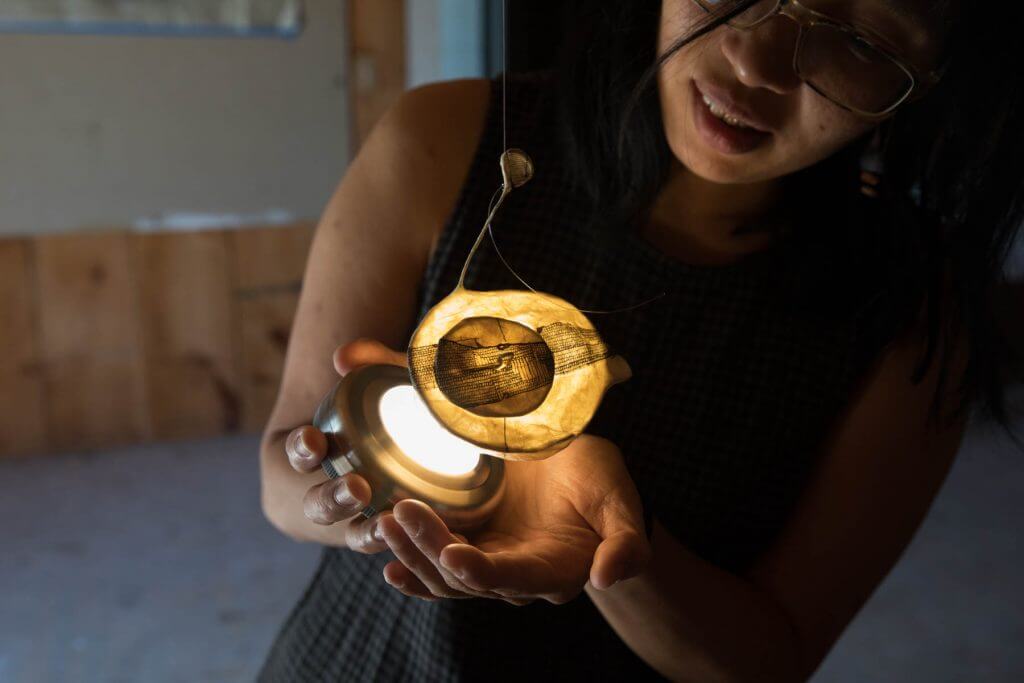 Person holding glowing yellow lantern or light in warm indoor setting