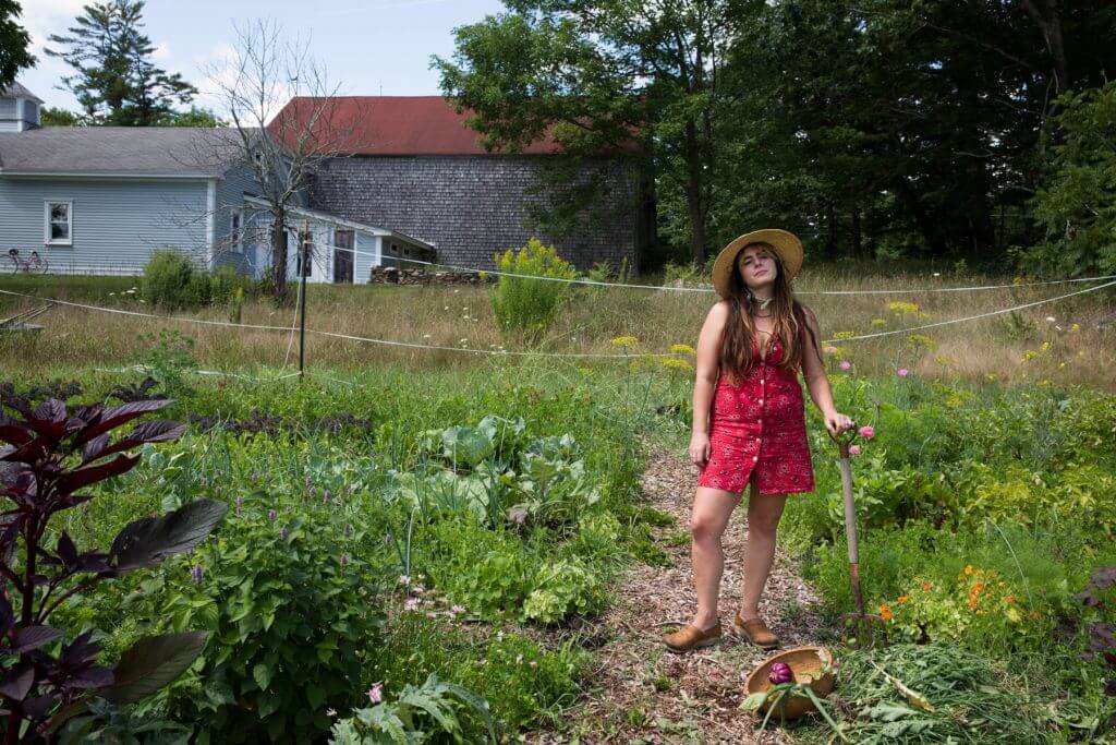 Woman in red dress and straw hat standing in lush vegetable garden