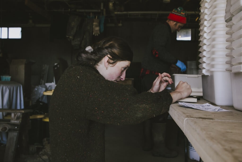 Person in dark sweater working intently at wooden desk in dim workshop