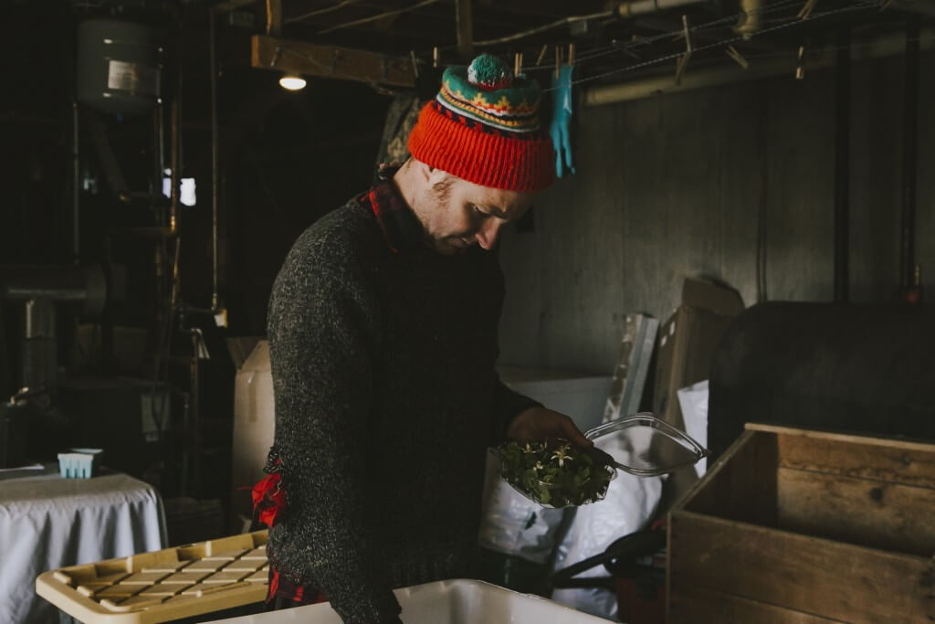 Person in colorful knit hat preparing food in dimly lit kitchen workspace