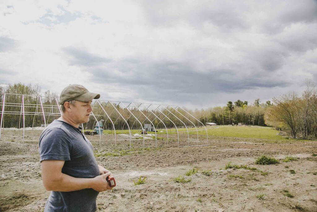 Farmer standing near empty greenhouse frames on an overcast day