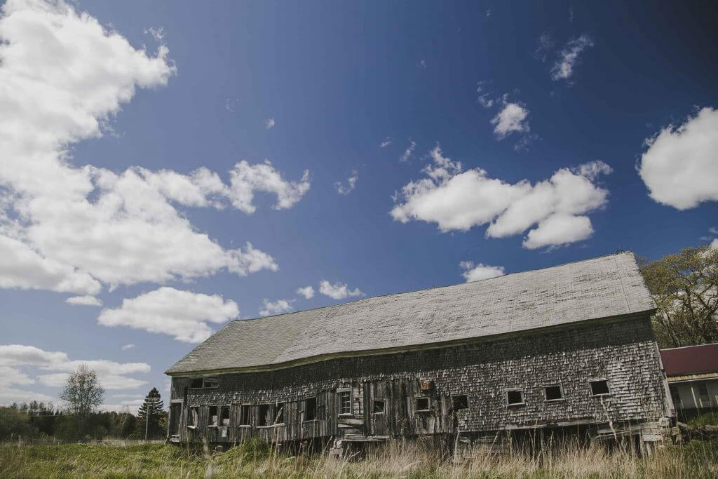 Weathered wooden barn in grassy field under fluffy white clouds