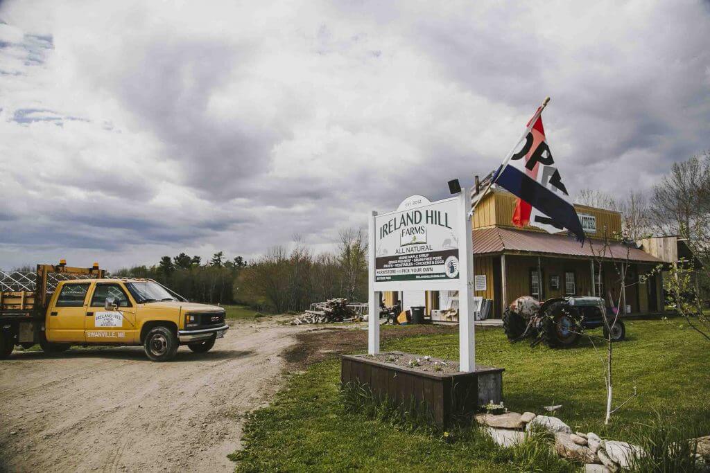 Ireland Hill Farms sign with yellow truck on dirt road under cloudy sky
