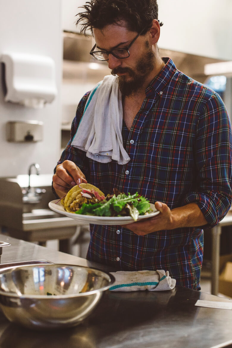 Chef in plaid shirt prepares taco with salad in kitchen