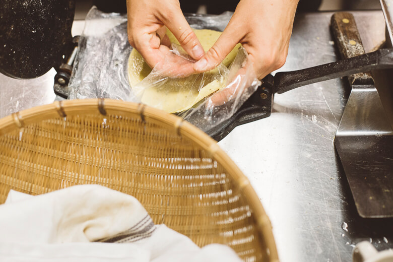 Hands preparing dough with plastic wrap on kitchen counter