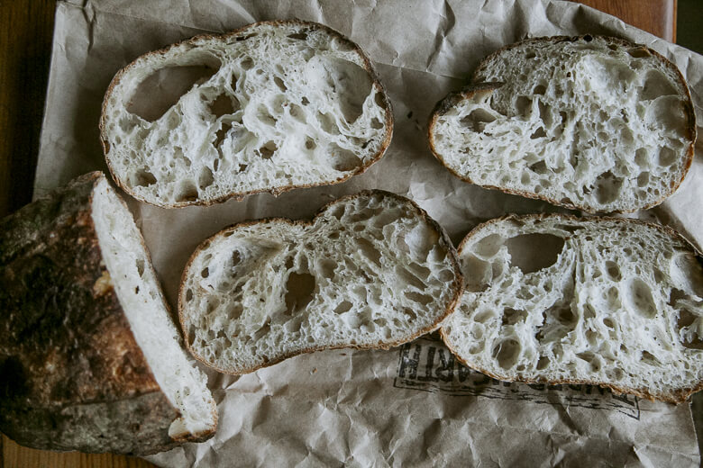 Rustic artisan bread slices with large, airy holes on crumpled paper