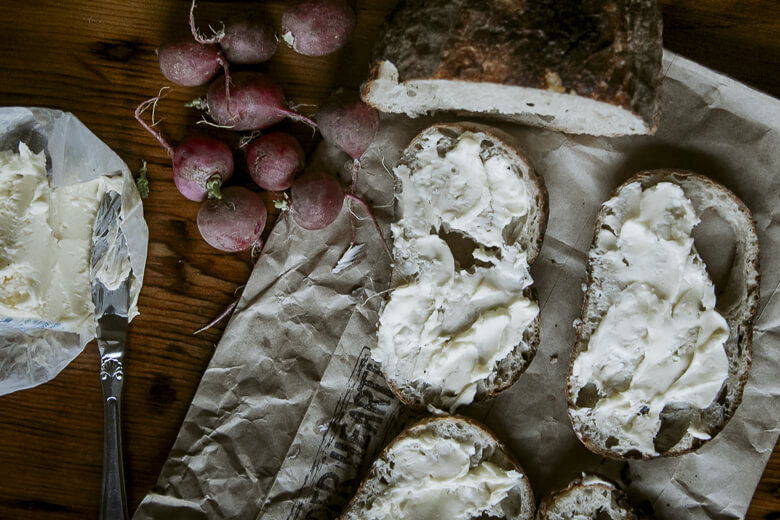 Radishes and bread slices spread with creamy cheese on crumpled paper