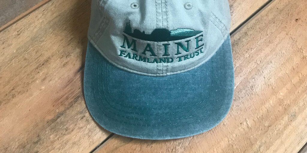 Maine Parkland Trust baseball cap in blue-green tones on wooden surface