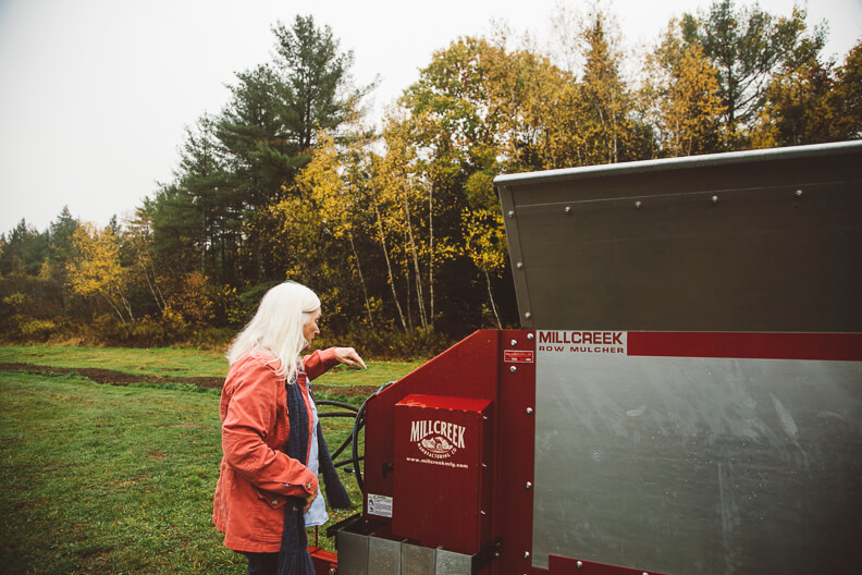 Person in red jacket operating Millcreek mulcher near autumn trees