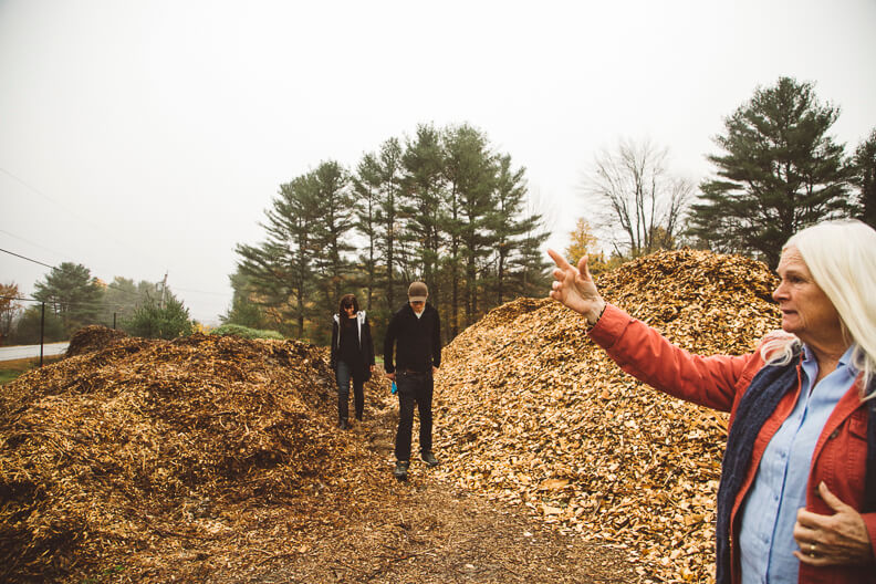 Woman gestures near large piles of autumn leaves with two people nearby