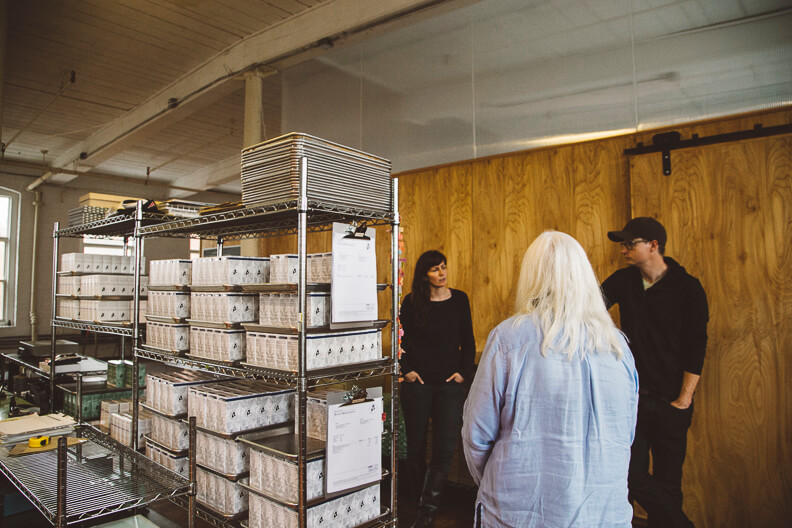 Storage room with metal shelves stacked with boxes and three people talking
