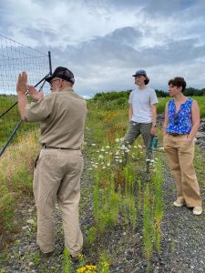 Three people standing near fence in grassy field under cloudy sky