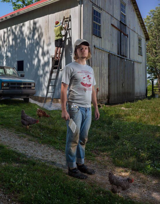 Person standing near barn with worker on ladder and chickens