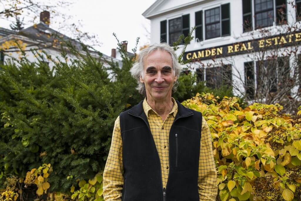 Smiling person in yellow shirt and black vest in front of Camden Real Estate