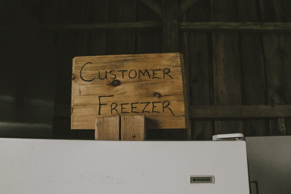 Handwritten wooden sign reading "Customer Freezer" above refrigerator