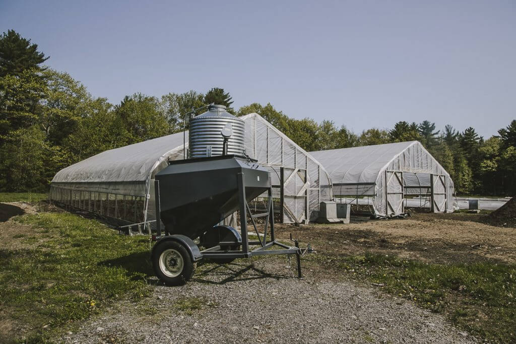 Agricultural greenhouse with water tank and trailer on gravel lot