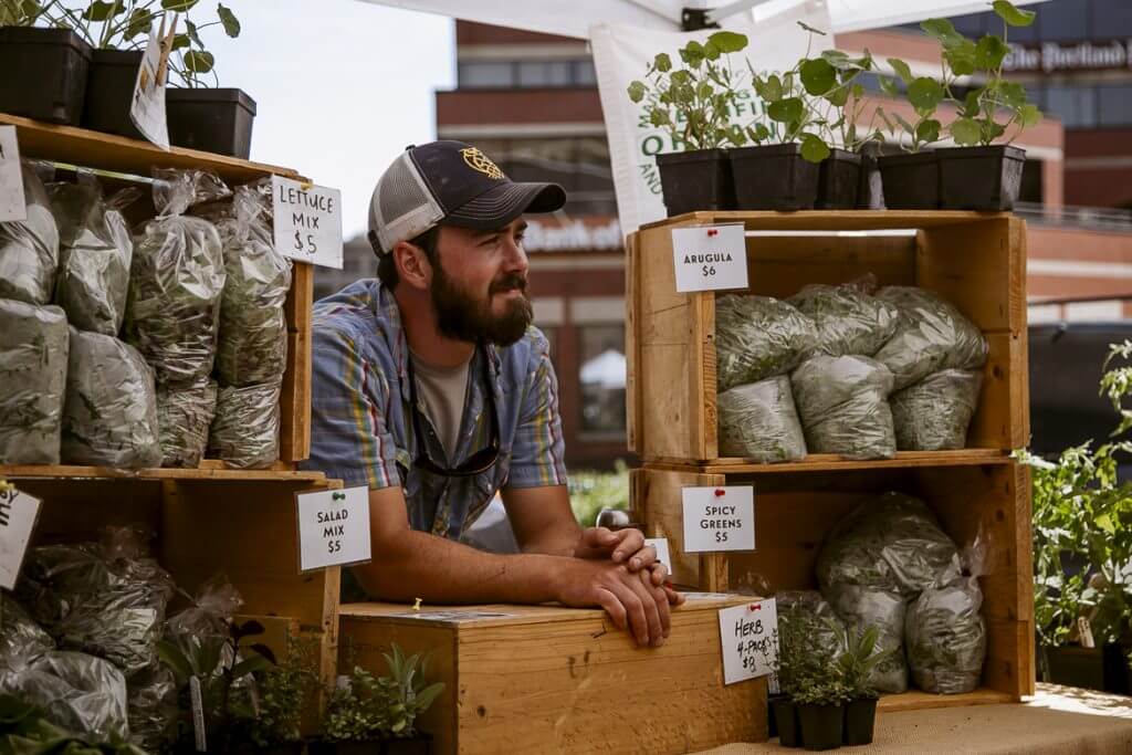Farmer selling fresh salad mix, greens, and herbs at local market stand