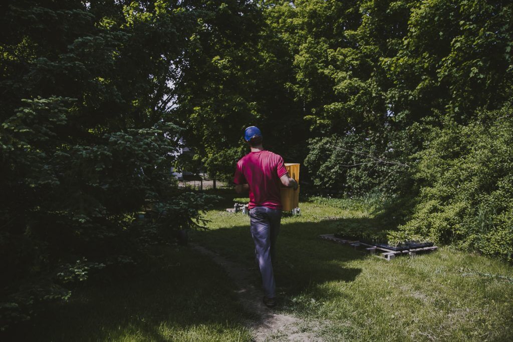 Person in pink shirt carrying yellow container walks through green forest path