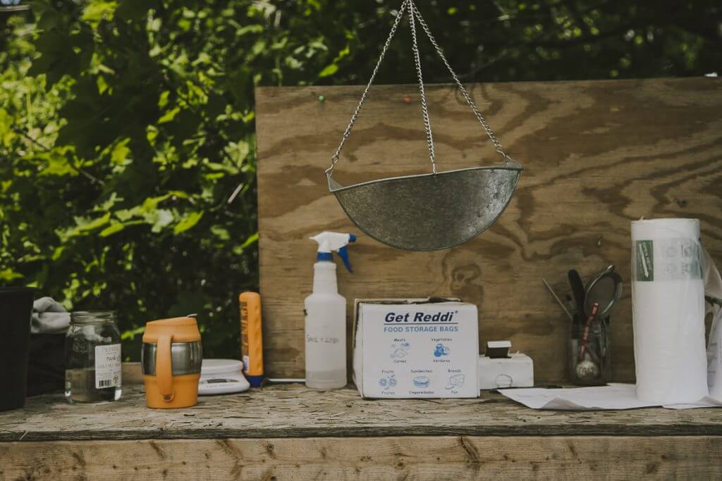 Outdoor wooden shelf with hanging strainer, spray bottle, and food storage supplies