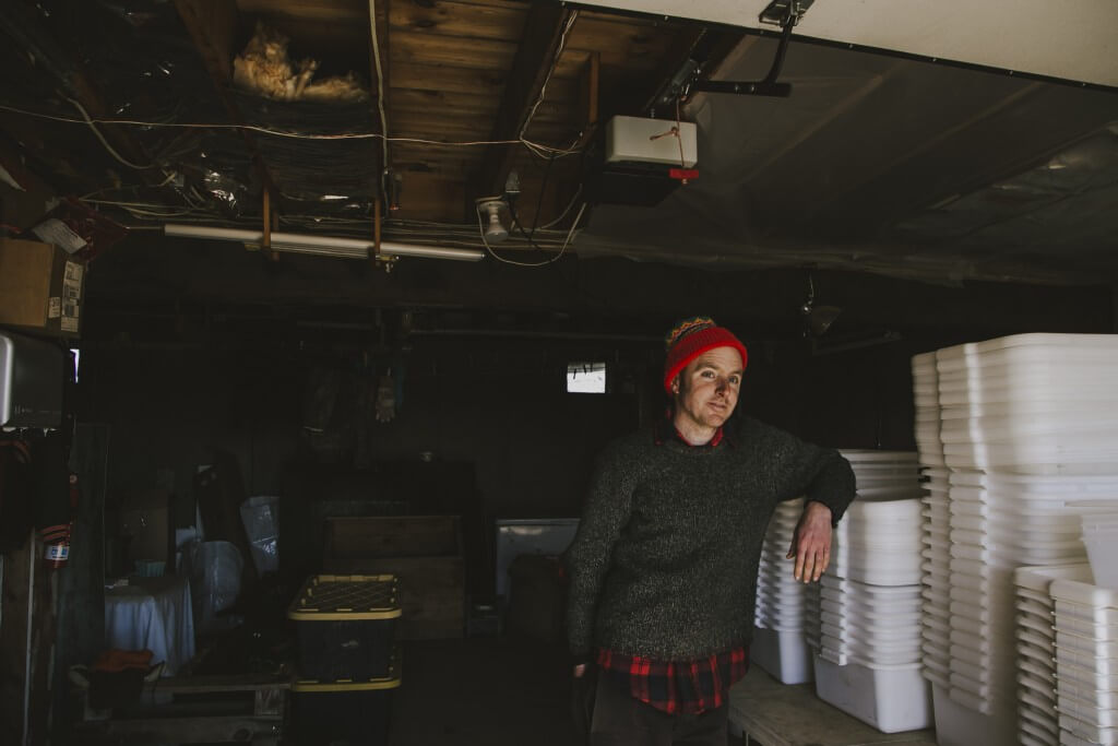 Person in red beanie standing in dimly lit storage room with stacked containers