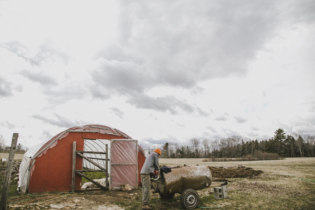 Red greenhouse with cloudy sky and agricultural equipment on rural farm