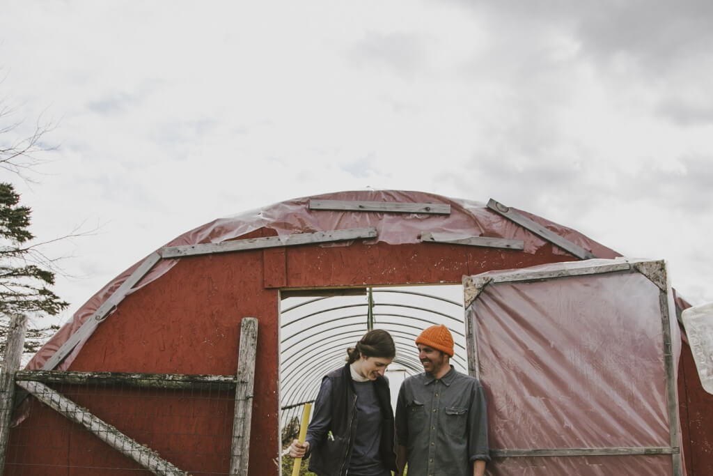 Two people stand near red agricultural greenhouse on cloudy day