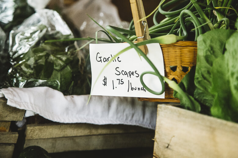 Garlic scapes for sale at $1.75 per bunch, displayed with green plants