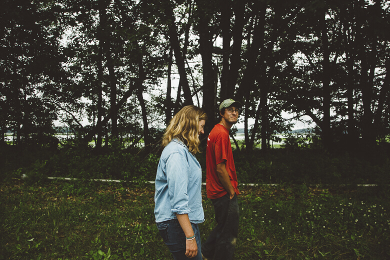 Two people standing side by side in a forest with trees and greenery