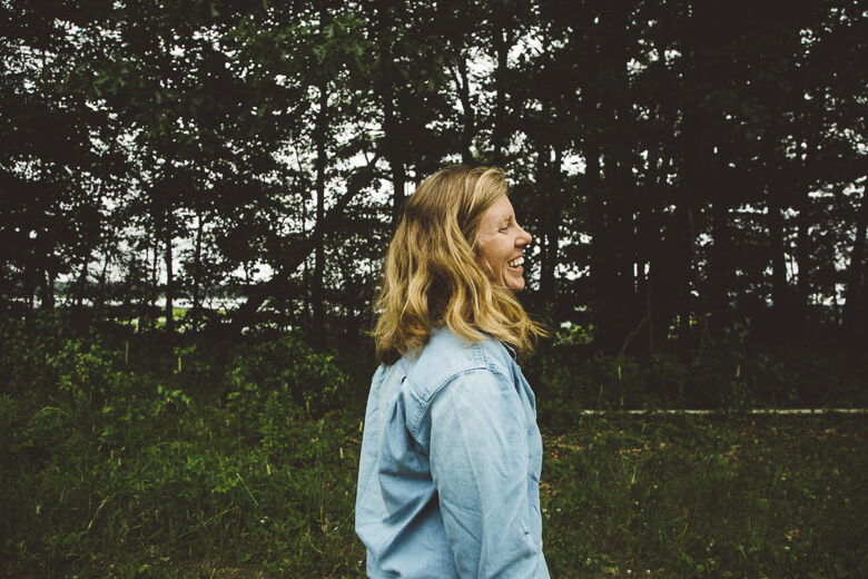 Woman laughing joyfully in forest with trees and greenery background