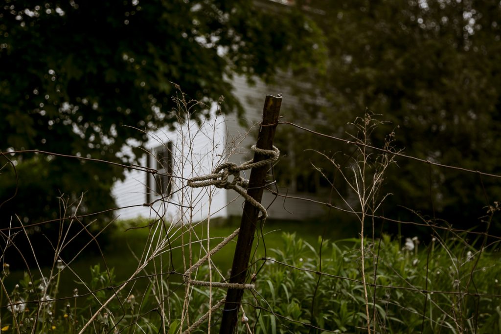 Weathered wooden fence post with twisted wire in overgrown grassy field