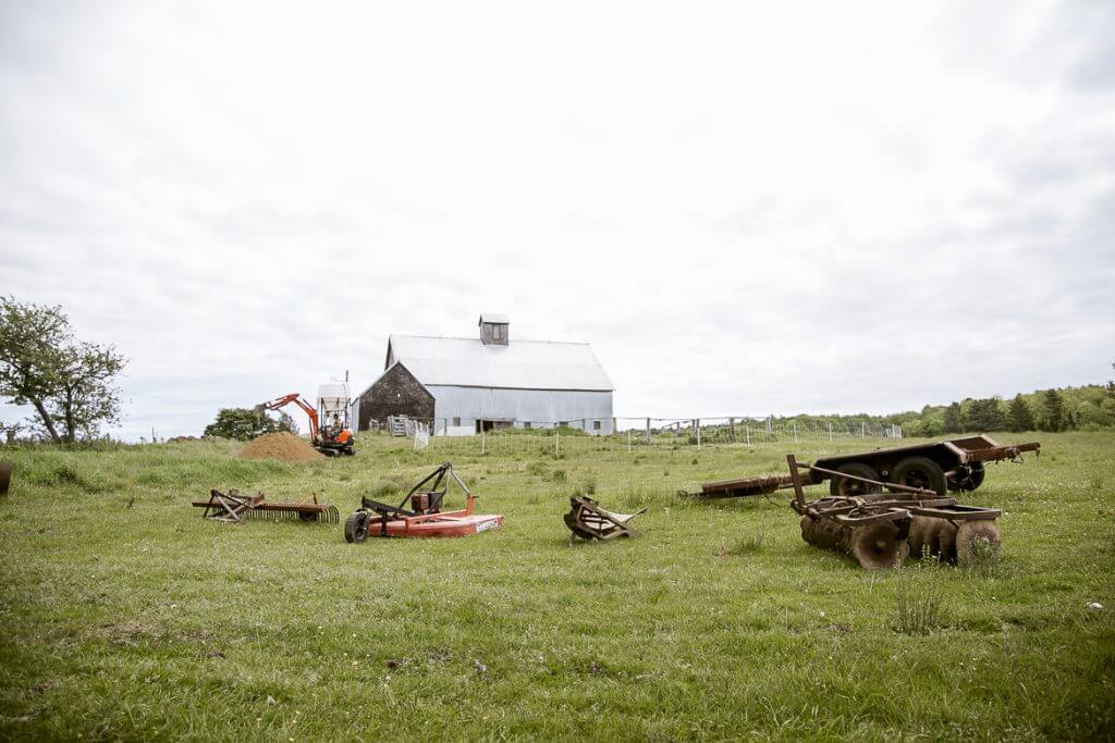 Vintage farm machinery scattered on green field with white barn