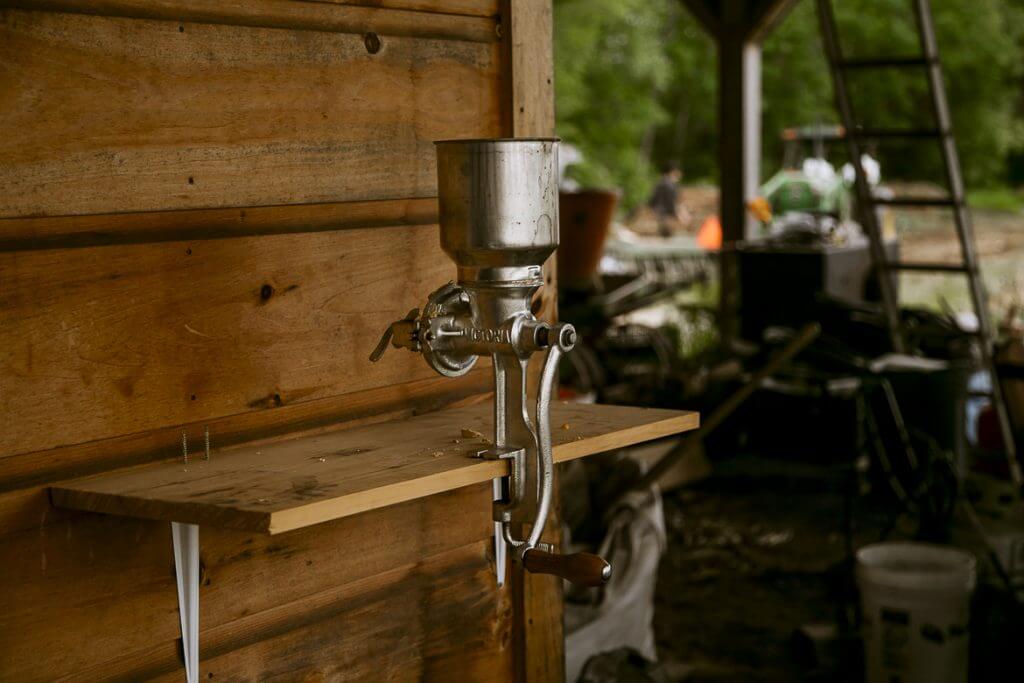 Vintage manual grain grinder mounted on wooden shelf in rustic workshop