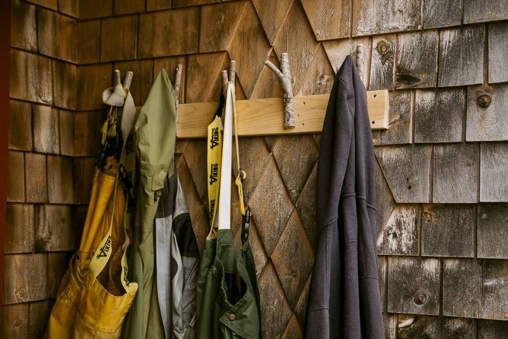 Coats and jackets hanging on wooden pegs against weathered shingle wall
