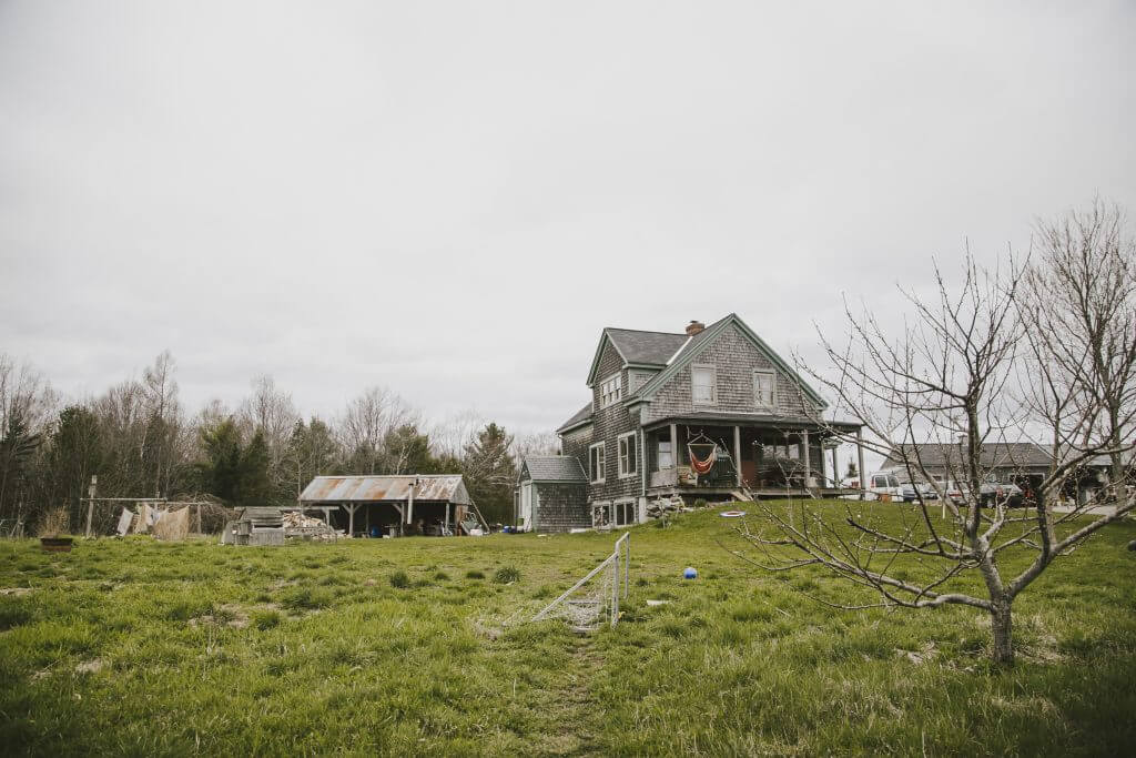 Old farmhouse with outbuilding on grassy land under cloudy sky