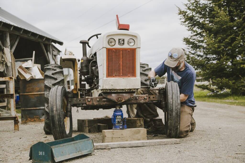 Farmer repairing vintage white and orange tractor using jack