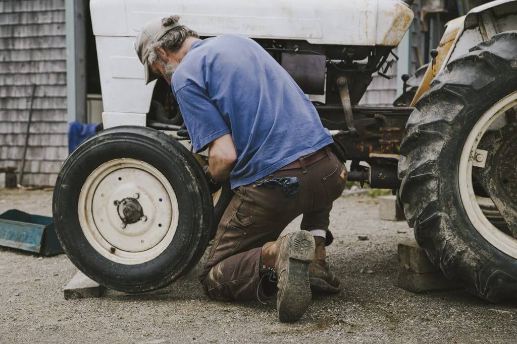 Farmer changing tire on old tractor near wooden shed