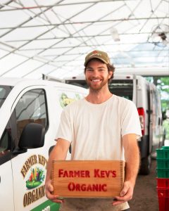 Smiling farmer holding Farmer Key's Organic sign next to delivery van