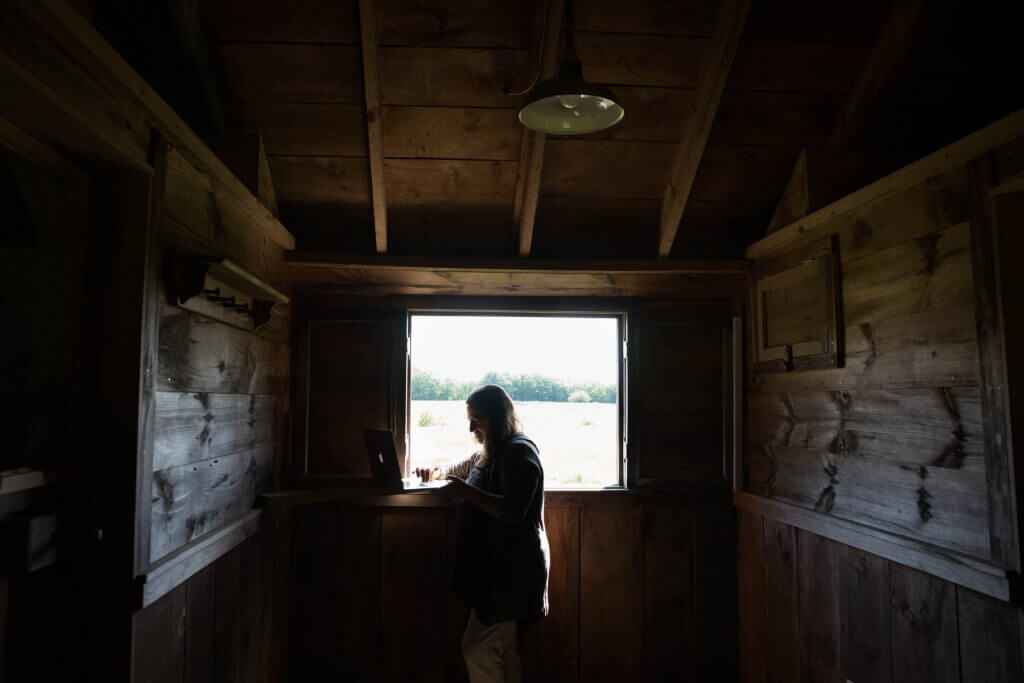 Silhouette of person looking out wooden cabin window into rural landscape