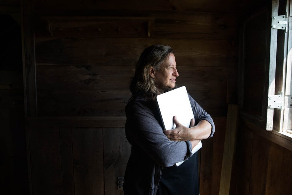 Person holding a white notebook, looking out wooden window thoughtfully