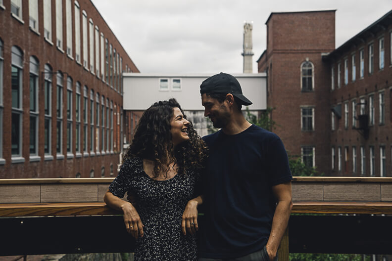 Couple laughing together on urban balcony with brick buildings behind