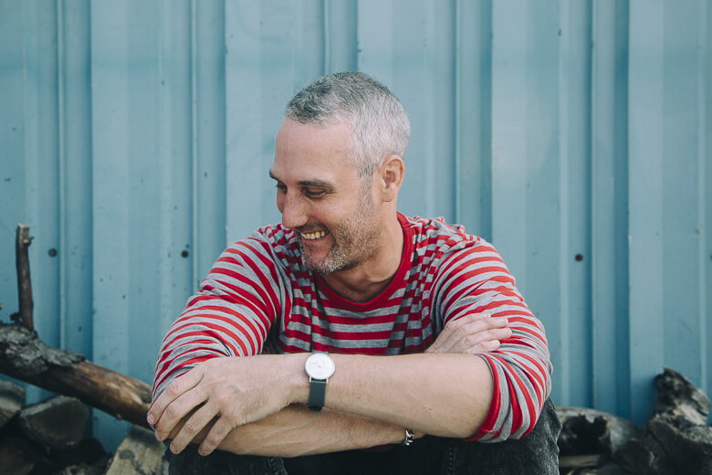 Smiling person in red and gray striped shirt leaning against blue wall