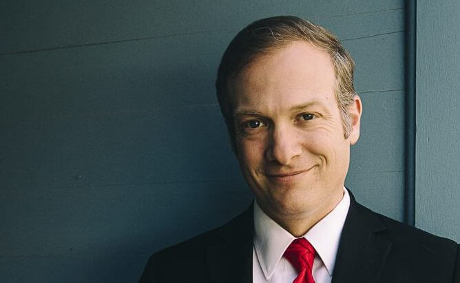 Professional businessman smiling in suit and red tie against gray background