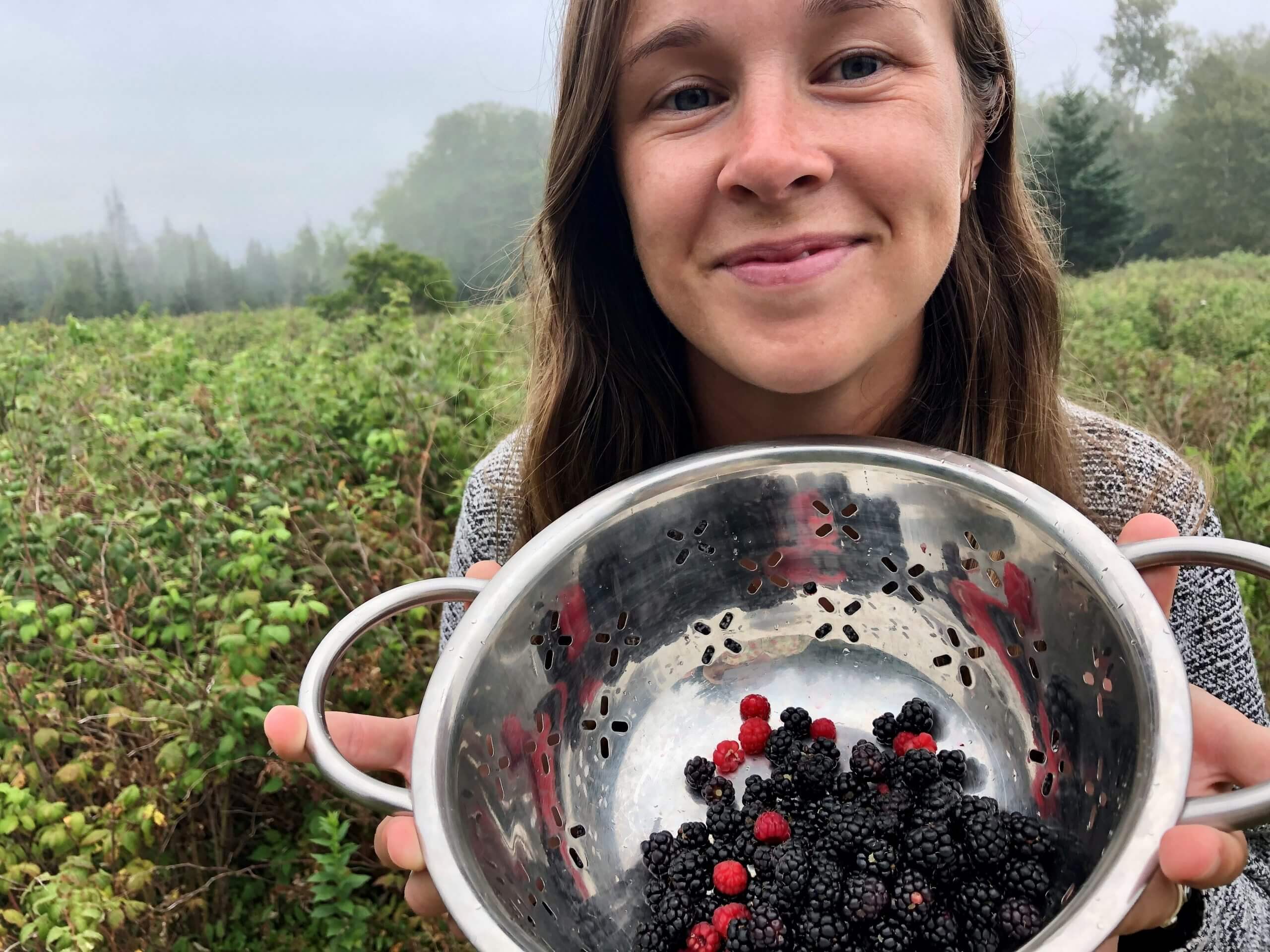 Smiling person holding colander with freshly picked blackberries and raspberries