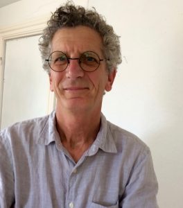 Smiling person with curly gray hair and glasses wearing a light blue shirt