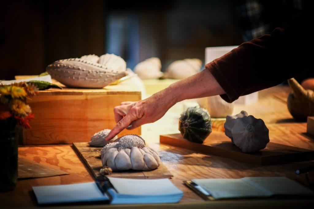 Hand arranging unusual carved stone or ceramic objects on wooden surface