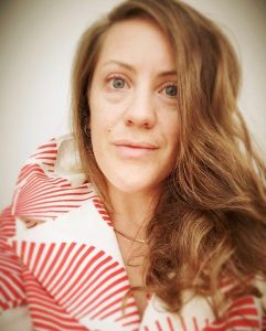 Woman in red and white striped top with long wavy hair looking sideways