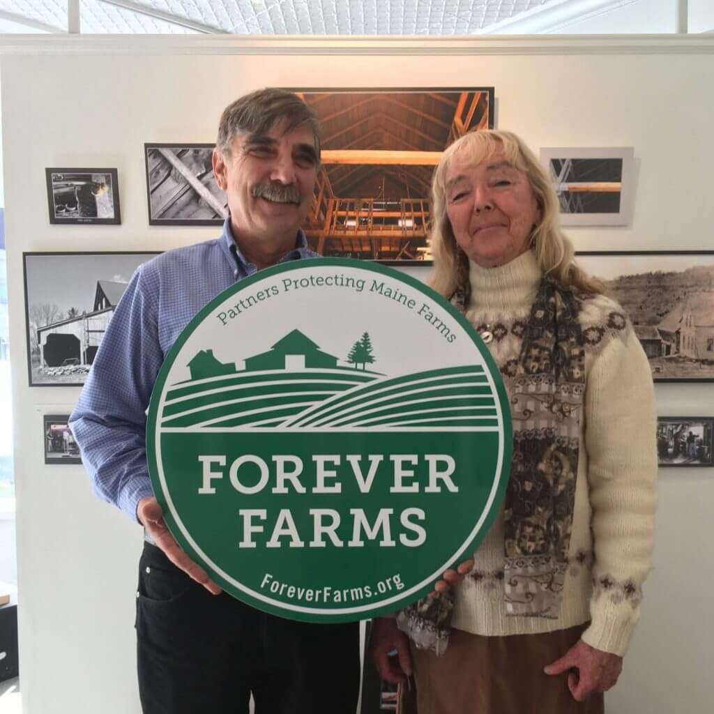 Two people holding Forever Farms sign supporting Maine agricultural preservation