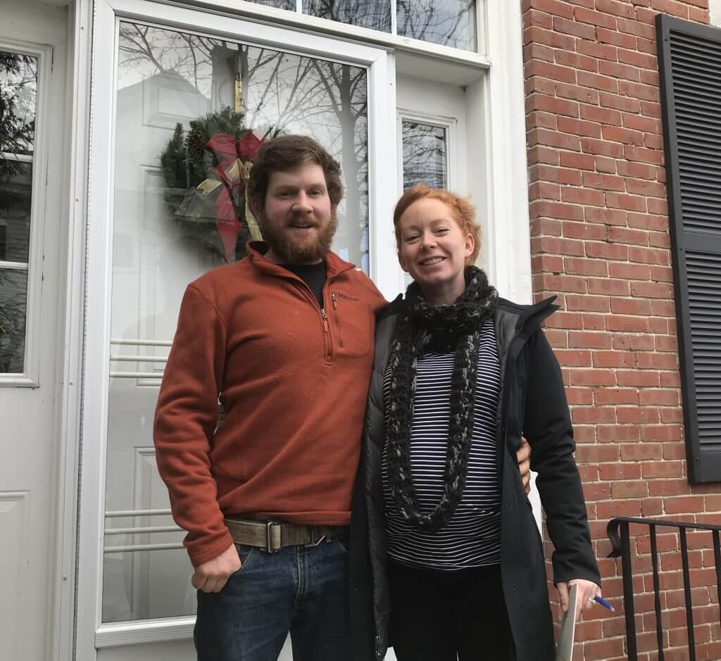 Couple standing in front of brick house with Christmas wreath